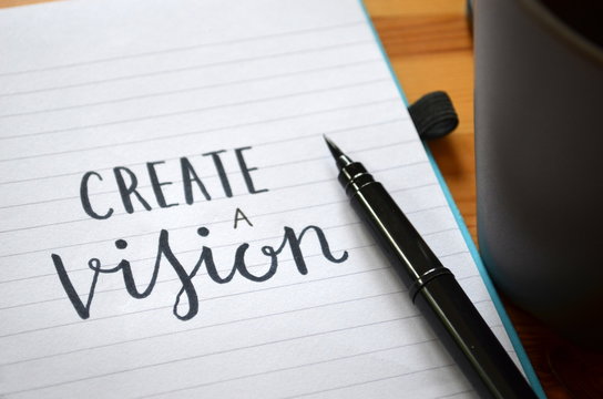 CREATE A VISION handwritten quote in notepad on desk with cup of coffee 