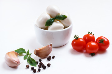 Cherry mozzarella in bowl, red cherry tomatoes, fresh basil, garlic and pepper on wight background