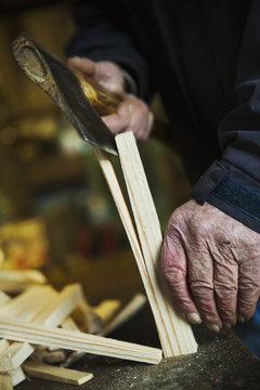 Close up of a man in a sailmaker's workshop splicing wooden pegs with a hand axe.
