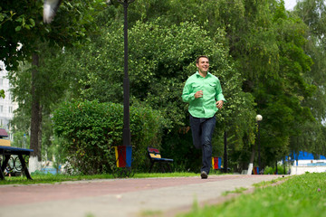 Young man in a green shirt and blue jeans running on summer park