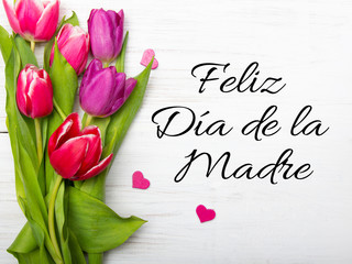 Mother's day card with Spanish words: Happy Mother's day, and  tulip bouquet on white wooden...
