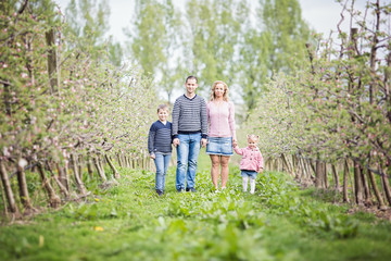 Happy young four member family standing together outdoors in orchard