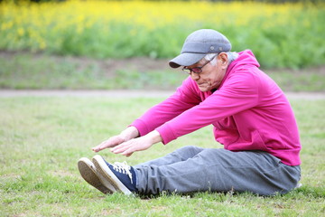 芝生の上で長座前屈をするシニアの男性