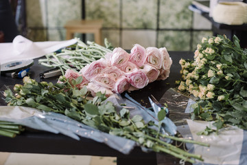 Florist workplace: tender fresh Ranunculus and little roses on the old wooden table with other greenery