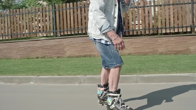 Tracking tilt up shot of senior hipster eating ice cream cone and listening to music through earphones while rollerblading down street in slow motion