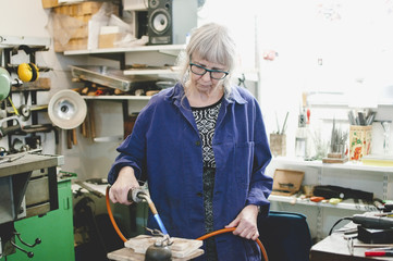 Senior craftsperson using blowtorch for metalworking in jewelry workshop