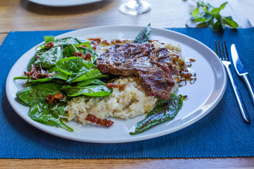 Gourmet restaurant lunch with tenderloin steak served on fresh spinach leaves with brown rice.  Horizontal view, white plate on a deep blue background.