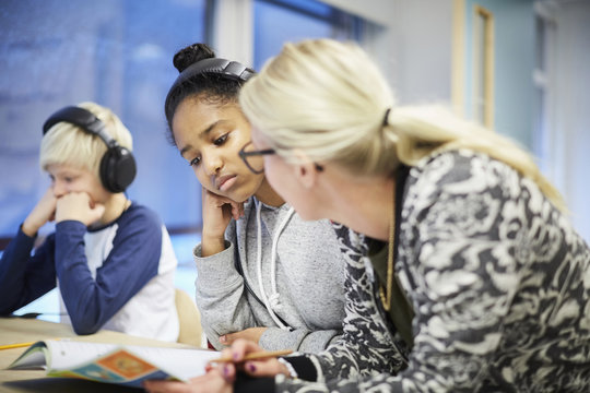 Girl wearing headphones while listening to teacher in classroom