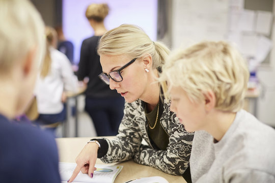 Teacher Reading Book To Students In Classroom