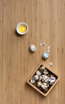 Farm guail eggs, whole and cracked on a wooden table.