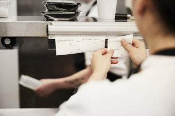 Cropped image of female chef reading order tickets in commercial kitchen