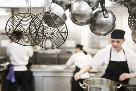 Kitchen utensils with chefs cooking in background at commercial kitchen