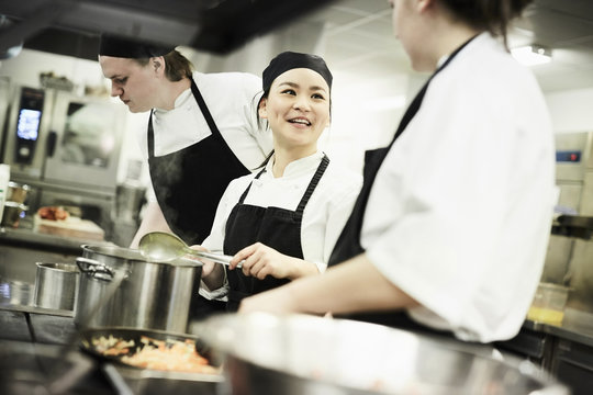 Female chef cooking food while talking with colleague in commercial kitchen
