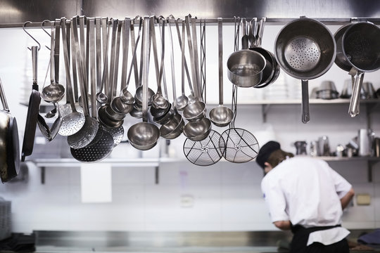 Utensils on metal rack with chef cooking in background at commercial kitchen