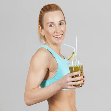 middle-aged athletic slim woman drinking the fresh fruit juice and smiling on the grey background