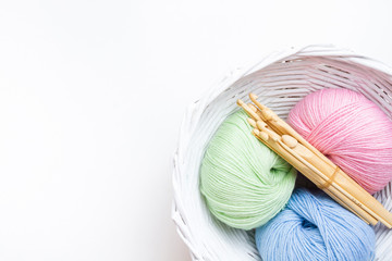 Pastel colored yarn in white basket and wooden crochet hooks of different sizes. Copy space.