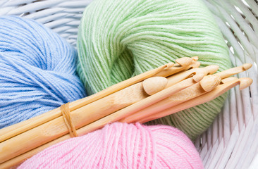 Pastel colored yarn in white basket and wooden crochet hooks of different sizes. - obrazy, fototapety, plakaty