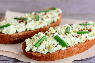 Guacamole sandwiches on paper and old wooden table. Healthy open rye sandwiches with sauce guacamole, fresh green onion and dried herbs on a paper. Vegan sandwiches photo. Closeup