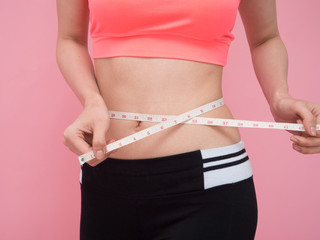 Slim young woman measuring her thin waist with a tape measure, close up
