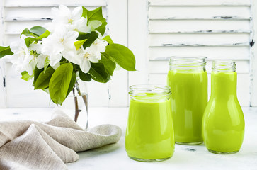 Detox, healthy green smoothie in jars and bottle. White wooden rustic background with apple blossom