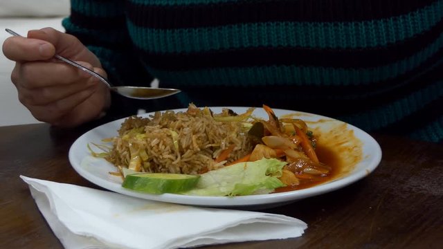 Woman enjoying Malaysian cuisine, eating Paprik fried rice with mixed seafood, chicken and vegetables cooked with red sauce
