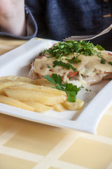 hands of the person eating the baked chicken under cheese from a white plate