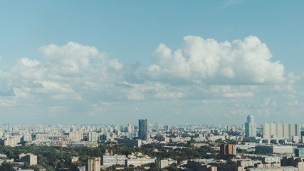 Sunny daylight metropolitan cityscape view from high point: residential and office buildings, business skyscrapers in distance, park and beautiful cloudscape on blue sky