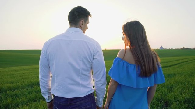 Back look of couple in love walking on the spring wheat field to sky horizon