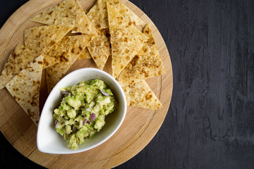 Green homemade Guacamole with chips. black background