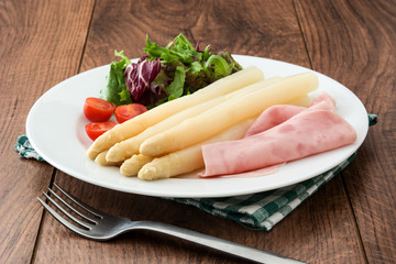White asparagus with salad and ham on wooden background
