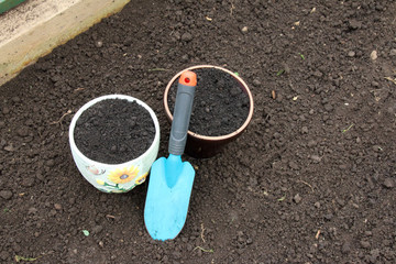 Ceramic flowerpots filled with the fresh soil for planting and a garden trowel in the polycarbonate greenhouse prepared for wintering