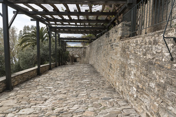 Fototapeta na wymiar Cobblestone road near stone walls, with wooden and ston archades, at seaside, in Greece, on The Holy Athos Mountain. Spring time.