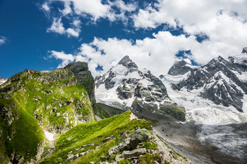 Summer mountain landscape with alpine meadow, glacier and rocky mountains with snow-capped summits. Greater Caucasus mountains in sunny day.