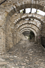 Cobblestone road near stone walls, with stone arcades, at seaside, in Greece, on The Holy Athos Mountain. Spring time.