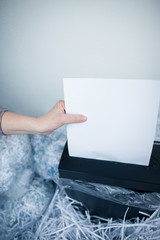 Senior woman hands shredding some white papers by automatic shredding machine (color toned image)
