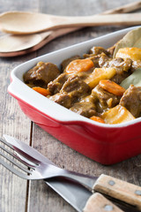 Beef meat stewed with potatoes, carrots and spices in ceramic pot on wooden table
