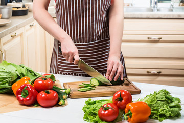 Young woman cooking in the kitchen at home. A woman cuts a cucumber and vegetables with a knife.