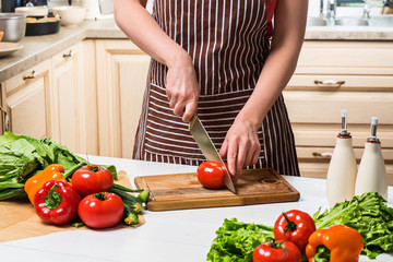 Young woman cooking in the kitchen at home. A woman cuts a tomato and vegetables with a knife.