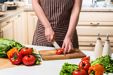 Young woman cooking in the kitchen at home. A woman cuts a tomato and vegetables with a knife.