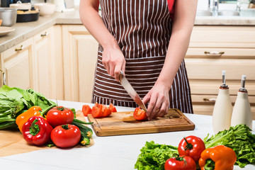 Young woman cooking in the kitchen at home. A woman cuts a tomato and vegetables with a knife.