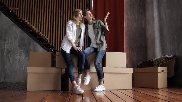 Girls Students Move to a New Apartment, Chatting Sitting on Boxes