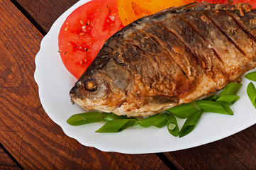 Roasted river fish carp on a white plate with tomatoes