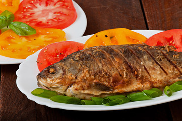Roasted river fish carp on a white plate with tomatoes
