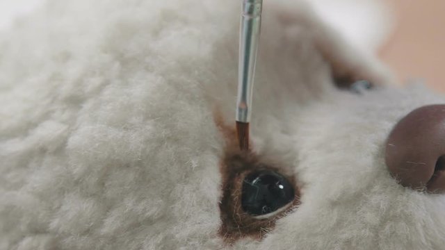 Process of creating a teddy bear: master draws a toy eyes. Thin brush for drawing: the eyes of a soft toy. Teddy bear in vintage style. Master paints eyes for a teddy bear in an old-fashioned style.