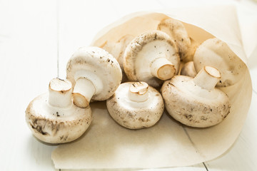 Freshly picked farm mushrooms champignons on a white wooden background in a paper bag.