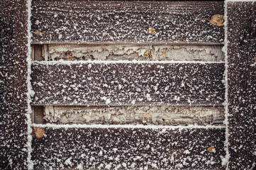 A wooden pallet covered with snow. Dry yellow autumn leaves.