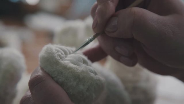 A thin brush in the hands of the artist to create soft toys. The toy is made in classic style. Fine brush for drawing: paws of a soft toy. The technology of creating a soft toy.