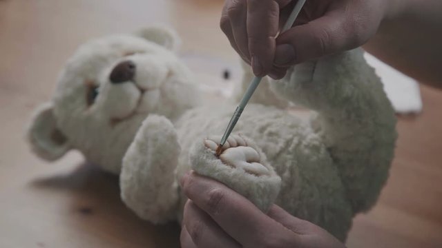 A thin brush in the hands of the artist to create soft toys. The master draws the dividers on the foot for a teddy bear in an old-fashioned style. Handmade teddy bear.