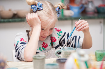 Little girl paints a piece of clay