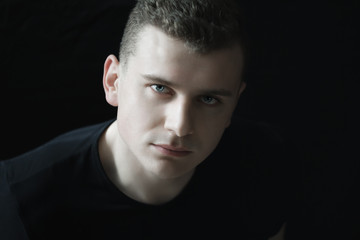 Headshot of confident young man is looking at camera in low-key lighting